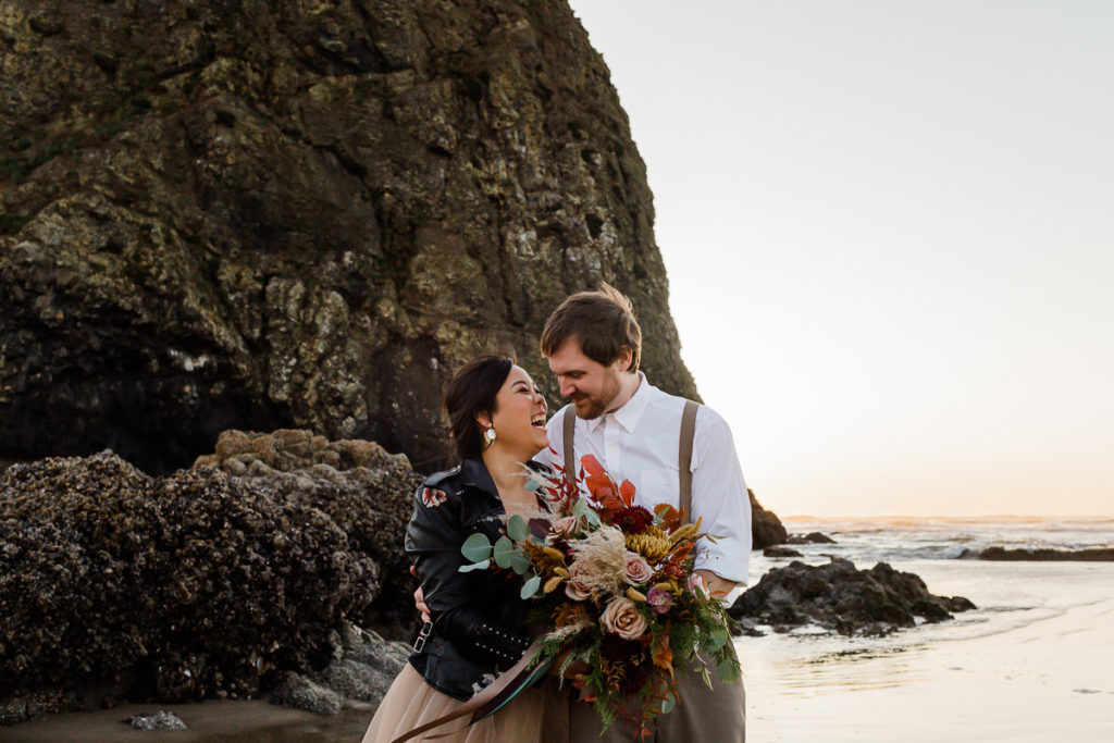 bride and groom laughing together in front of haystack rock