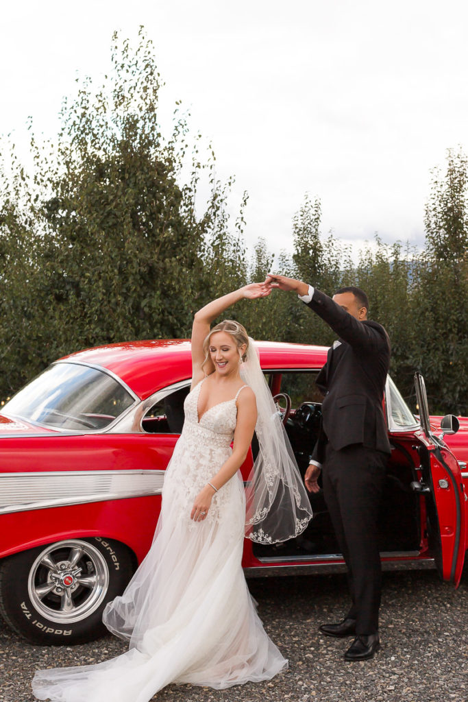 bride and groom posing with a classic red car
