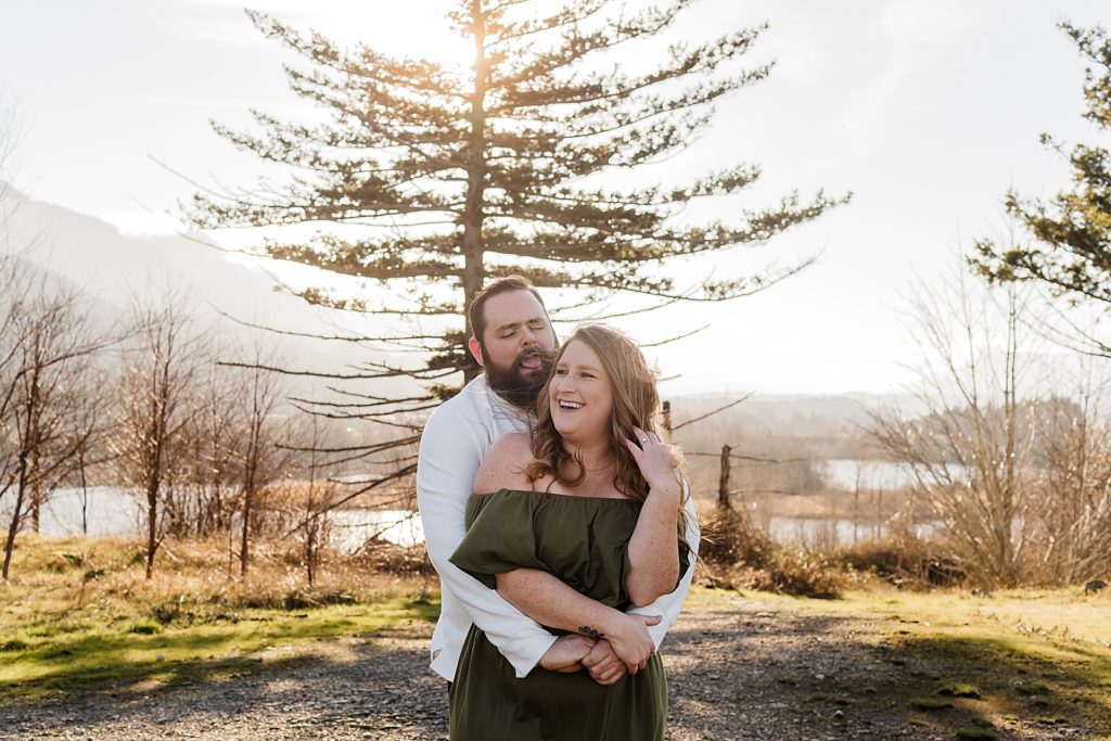 Man holding woman from behind and sticking his tongue out and goofying off Government Cove Oregon Engagement Photography captured by Oregon Engagement Photographer Simply Wandering Photography 