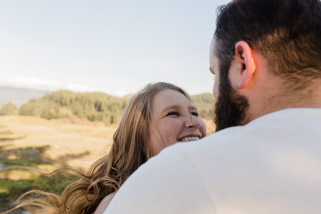 Woman looking at man with green pastures and trees behind them Government Cove Oregon Engagement Photography captured by Oregon Engagement Photographer Simply Wandering Photography 