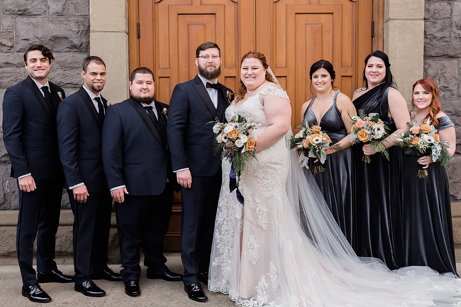 Bride and Groom standing together outside of church doors with Bridal party 