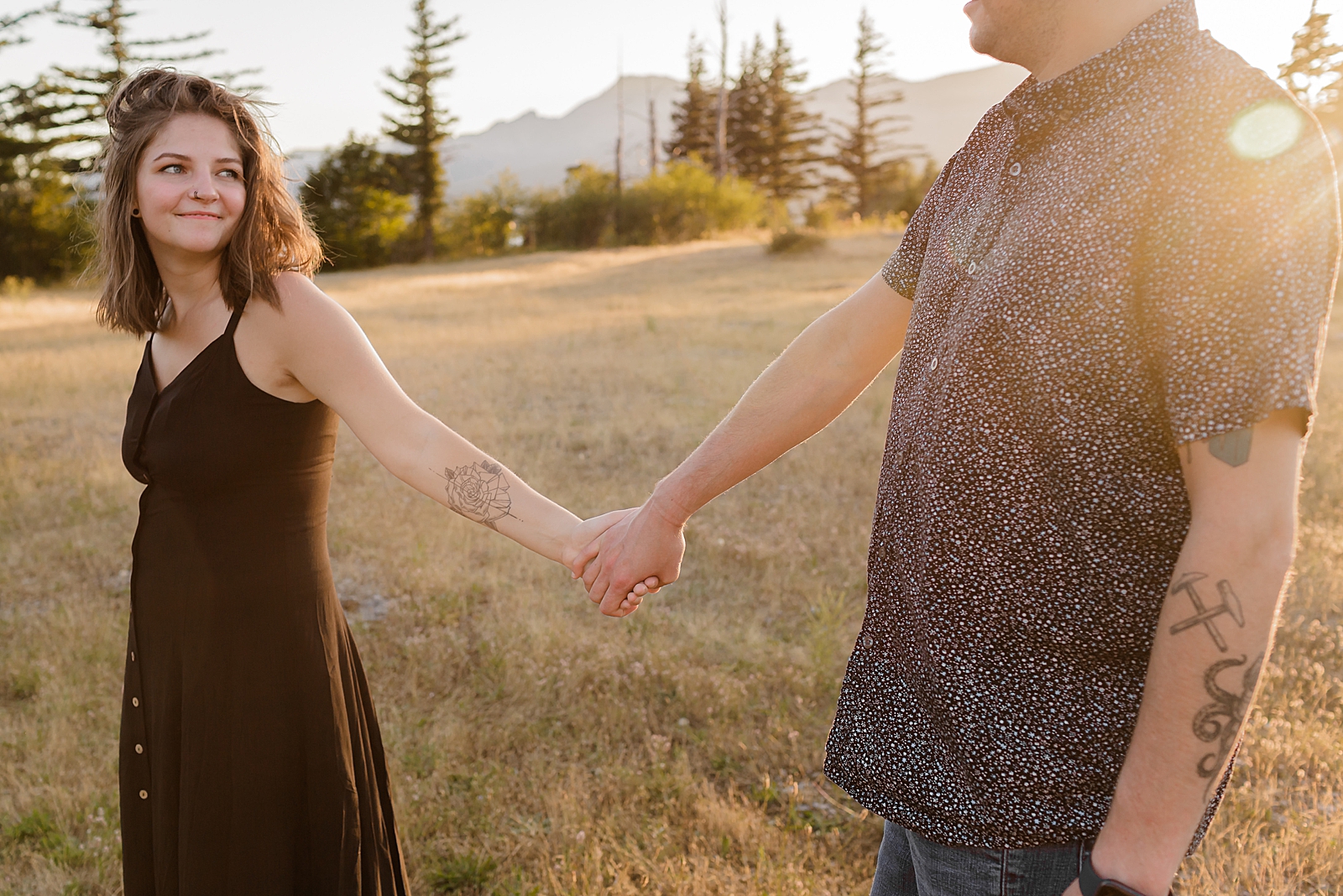 Couple holding hands and looking at each other on grassy field with the sun setting