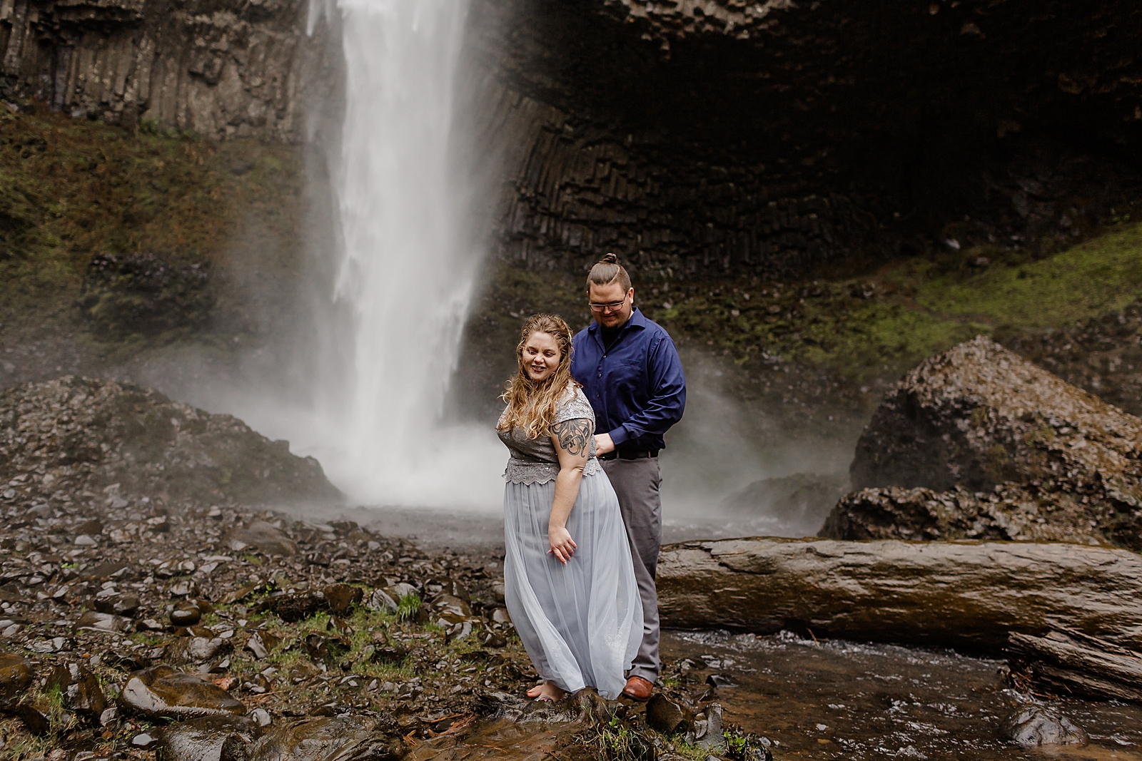 Couple walking on wet rock bottom of waterfall 