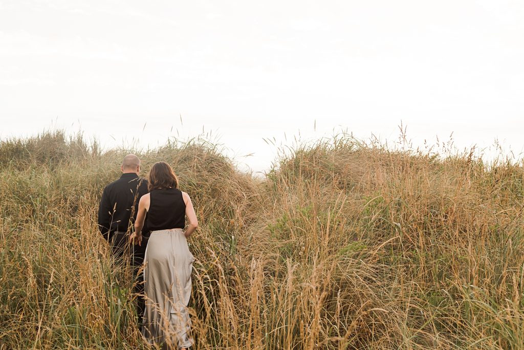 Couple holding hands navigating through tall grass hill