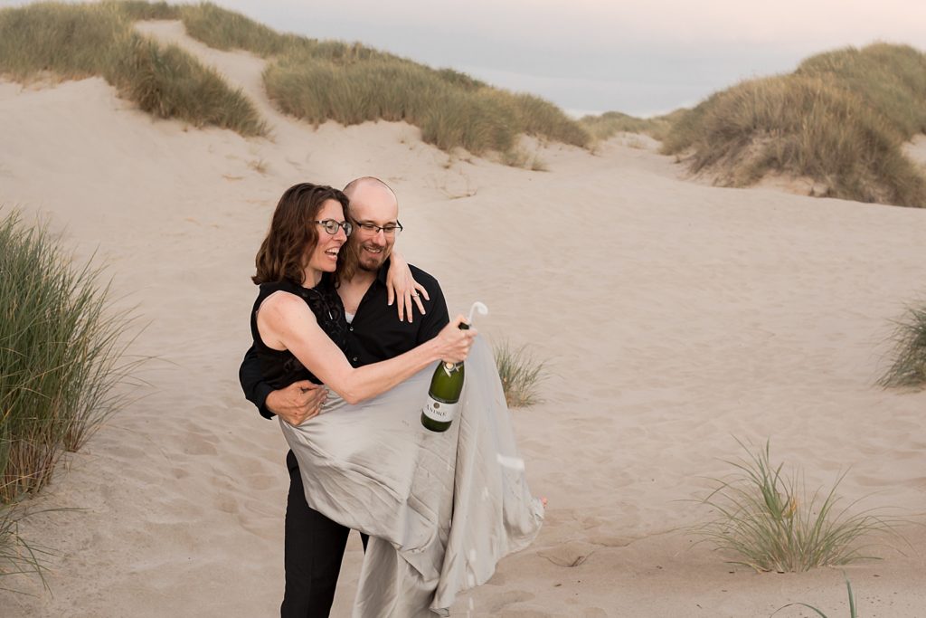 Man holding woman popping Champaign on the sand