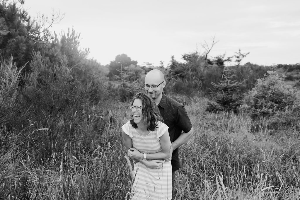 B&W of couple walking through tall grass field laughing