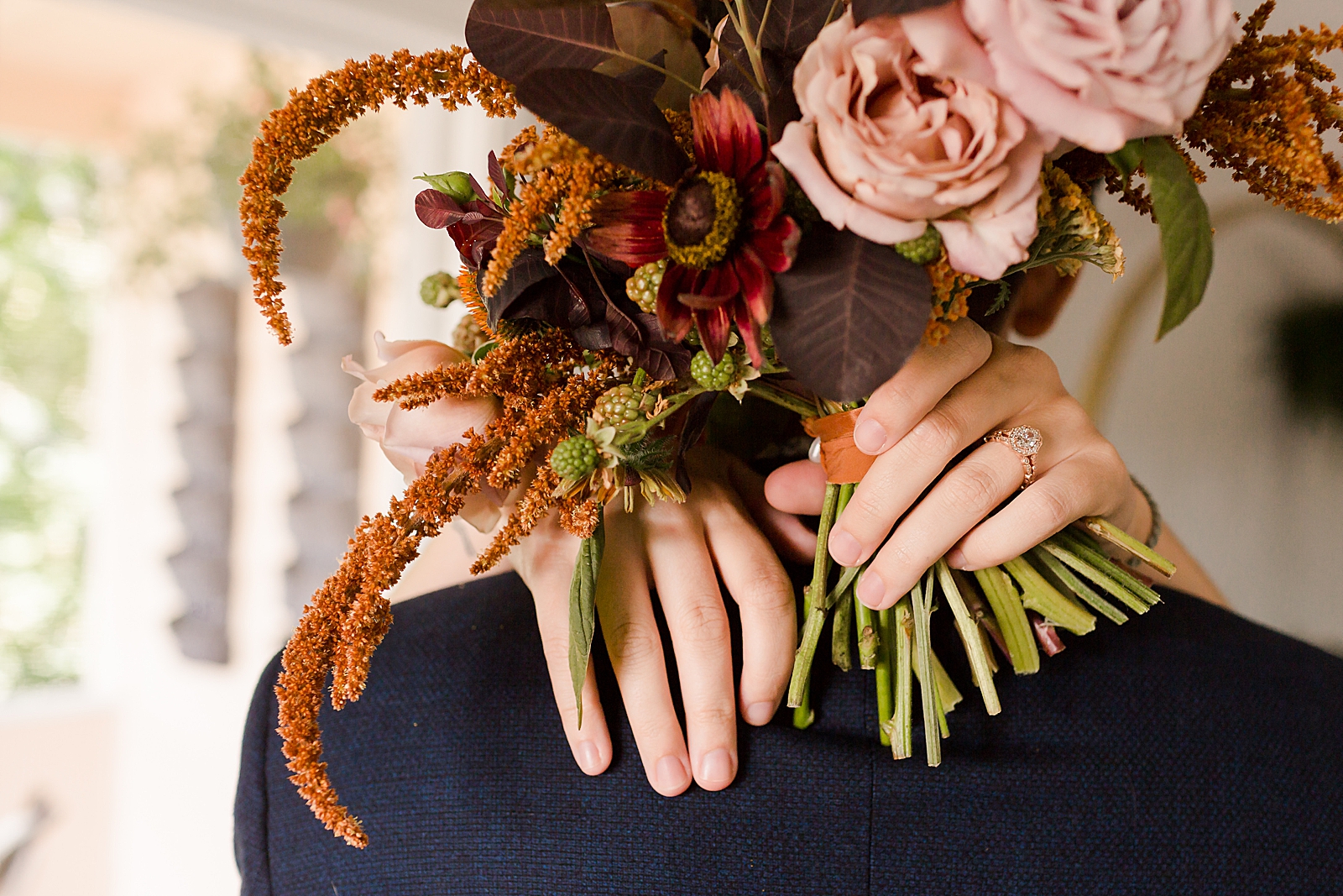 Closeup of Bride's arms around Groom holding bouquet and wearing extravagant engagement band 