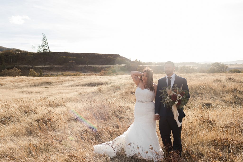Bride and Groom holding hands walking on dry grass field together the sun shining bright on them