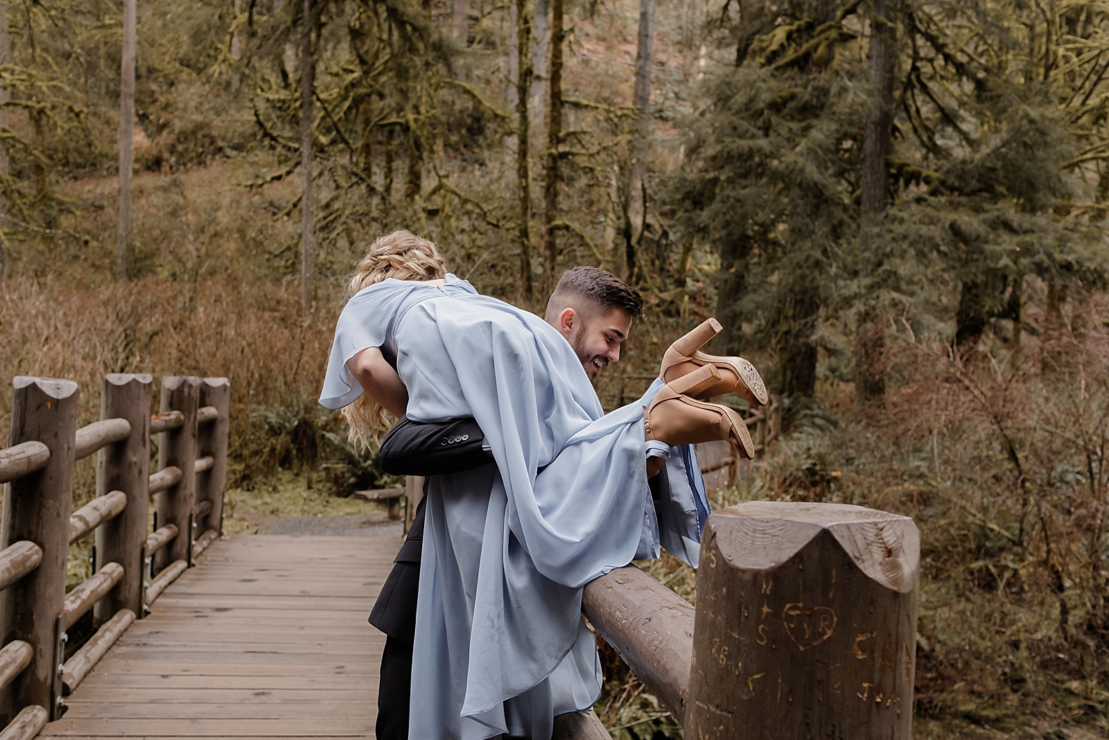 Man carrying woman over shoulder through the woods and over the bridge Silver Falls State Park Oregon Adventure Photography captured by Simply Wandering Photography 