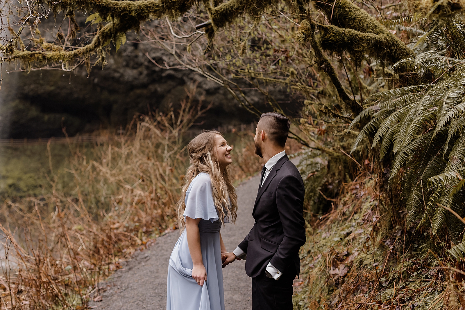 Couple holding hands and standing on sidewalk in the woods Silver Falls State Park Oregon Adventure Photography captured by Simply Wandering Photography 