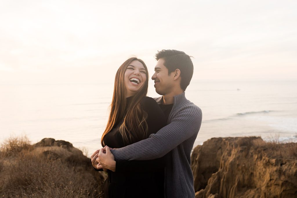 Couple laughing and holding each other in front of ocean water