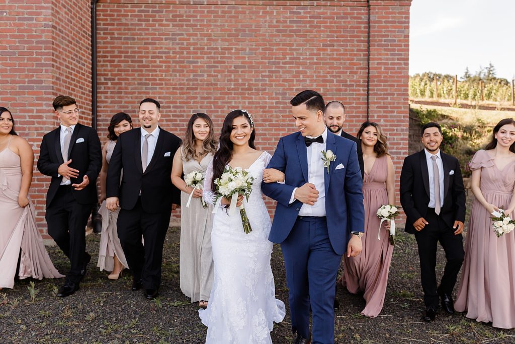 Bride and Groom arm in arm walking together with Bridal party following them