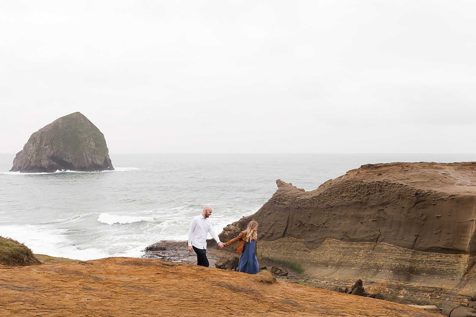 Couple holding hand and walking by canyon cliff with waves in the background