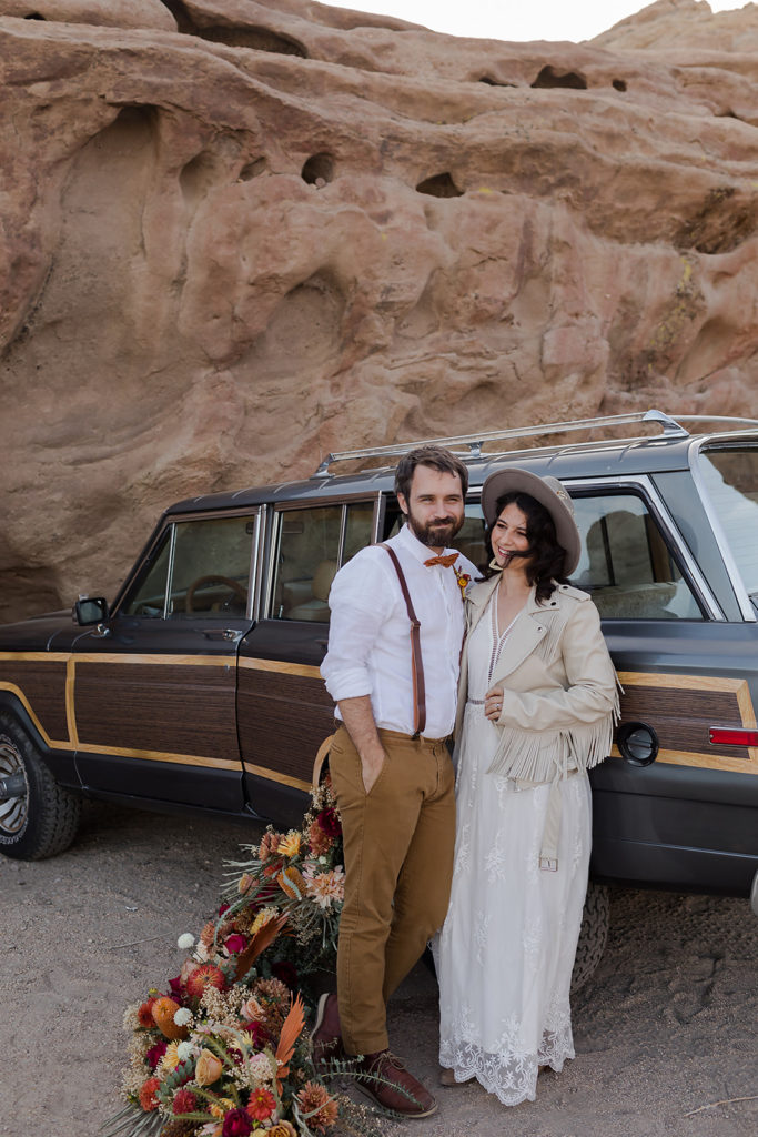 bride and groom leaning against classic jeep wagoneer